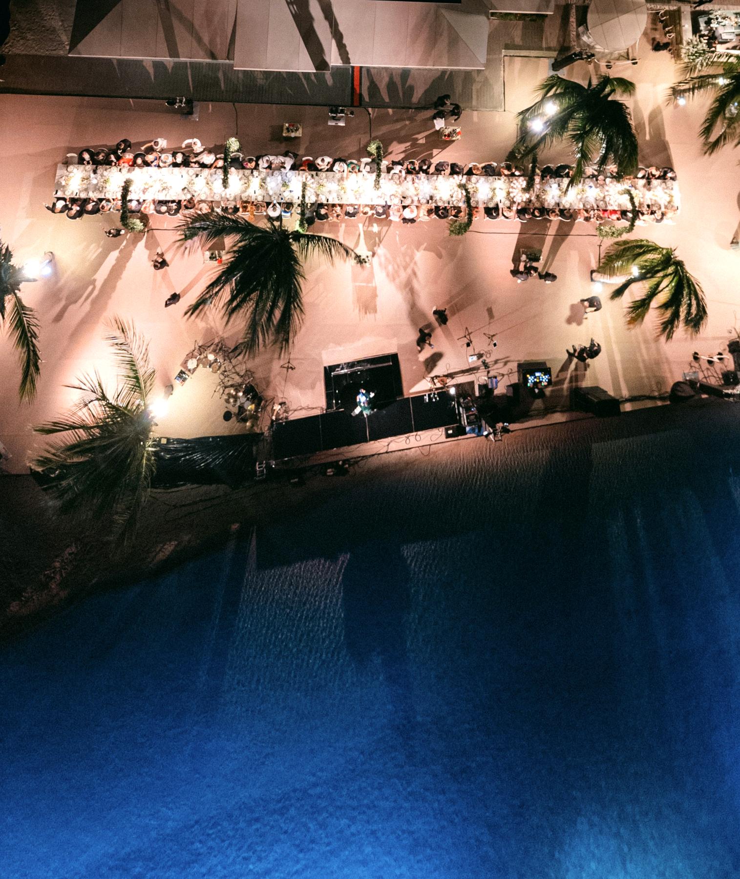 Aerial night view of a long-table beach wedding dinner by the sea with glowing chandeliers, Curacao