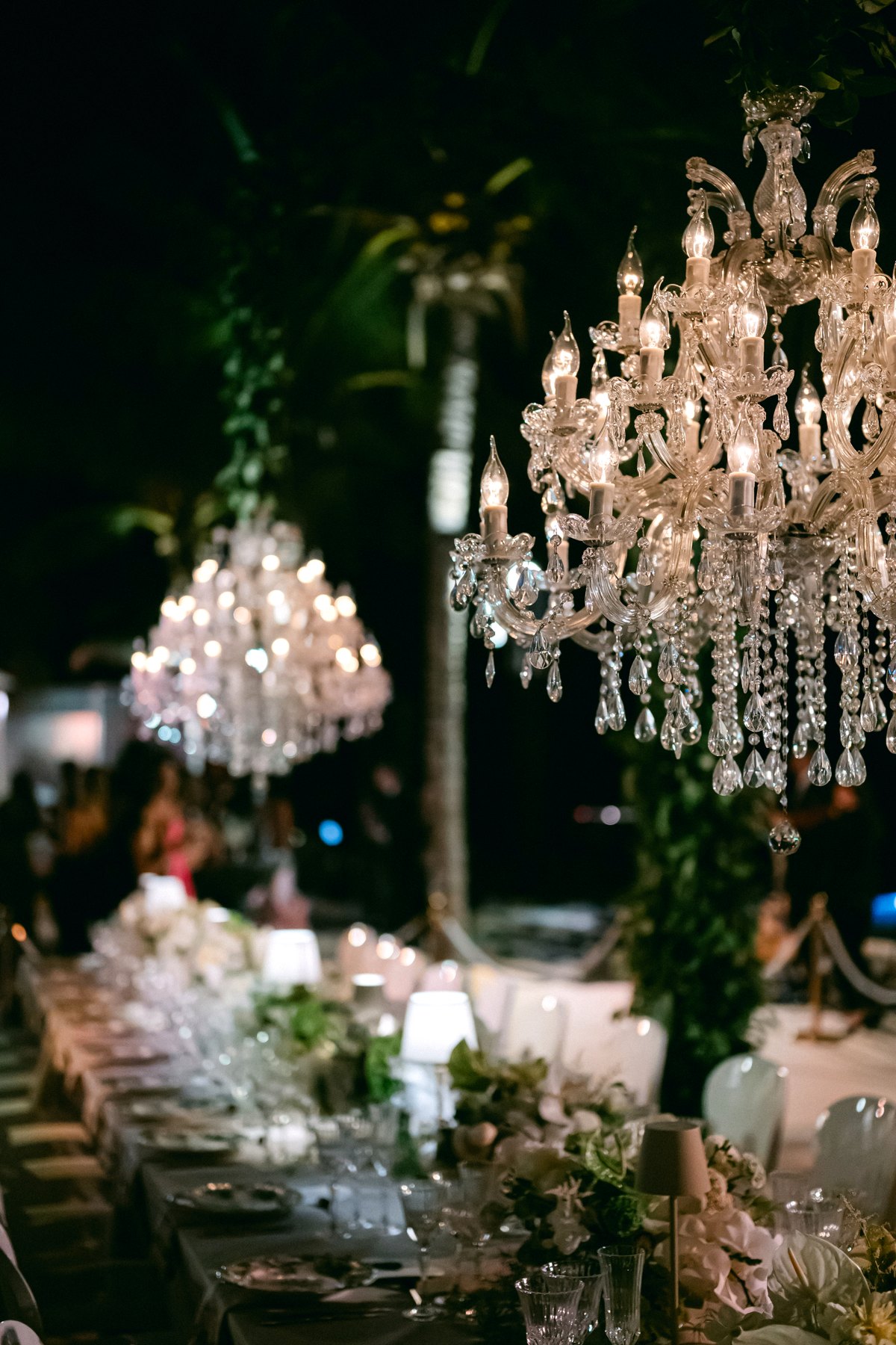 Crystal chandelier suspended from a greenery arch above a beach wedding table, Curacao