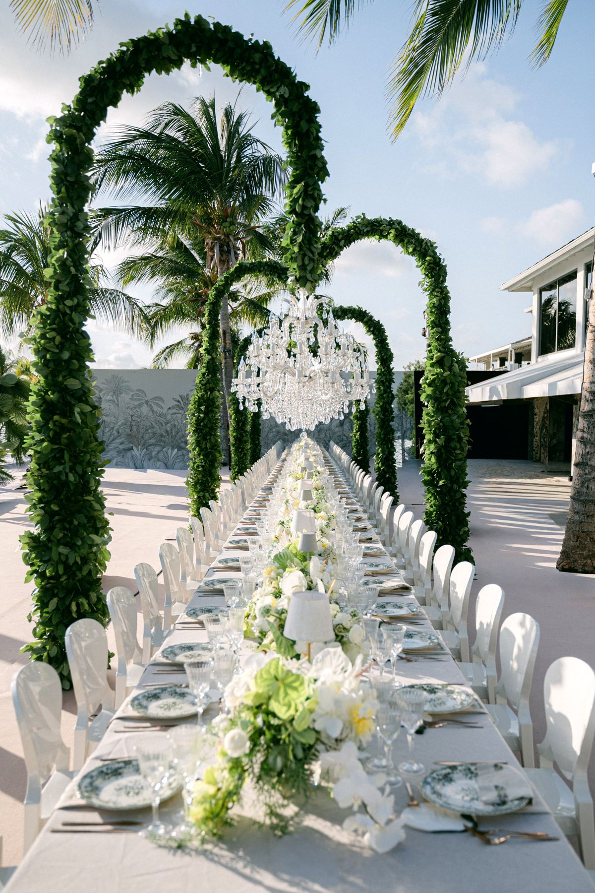 Full long wedding dinner table beneath greenery arches with crystal chandelier, Curacao beach wedding